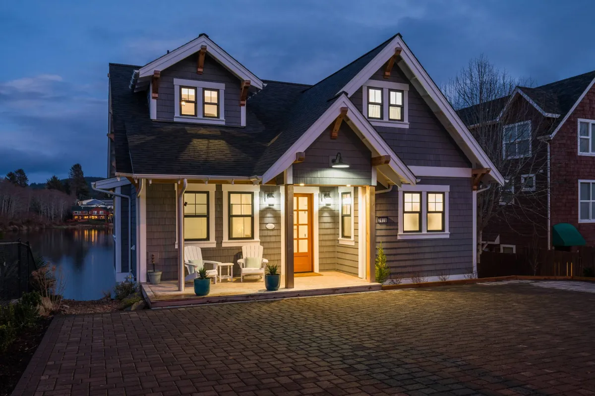 This image features the welcoming front porch and entryway of the home, set against beautifully landscaped surroundings with views of the water just beyond. The space is designed for gathering and relaxing outdoors, with ample seating and a sense of connection to the lake environment.