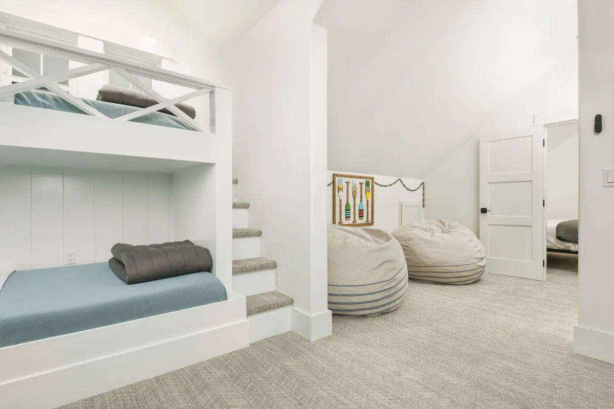A bright, cozy bunk room featuring bunk beds, colorful bean bags, and playful wall art. This space is designed for children and teens to relax, read, play games, or enjoy sleepovers, creating a fun and safe retreat within the home.