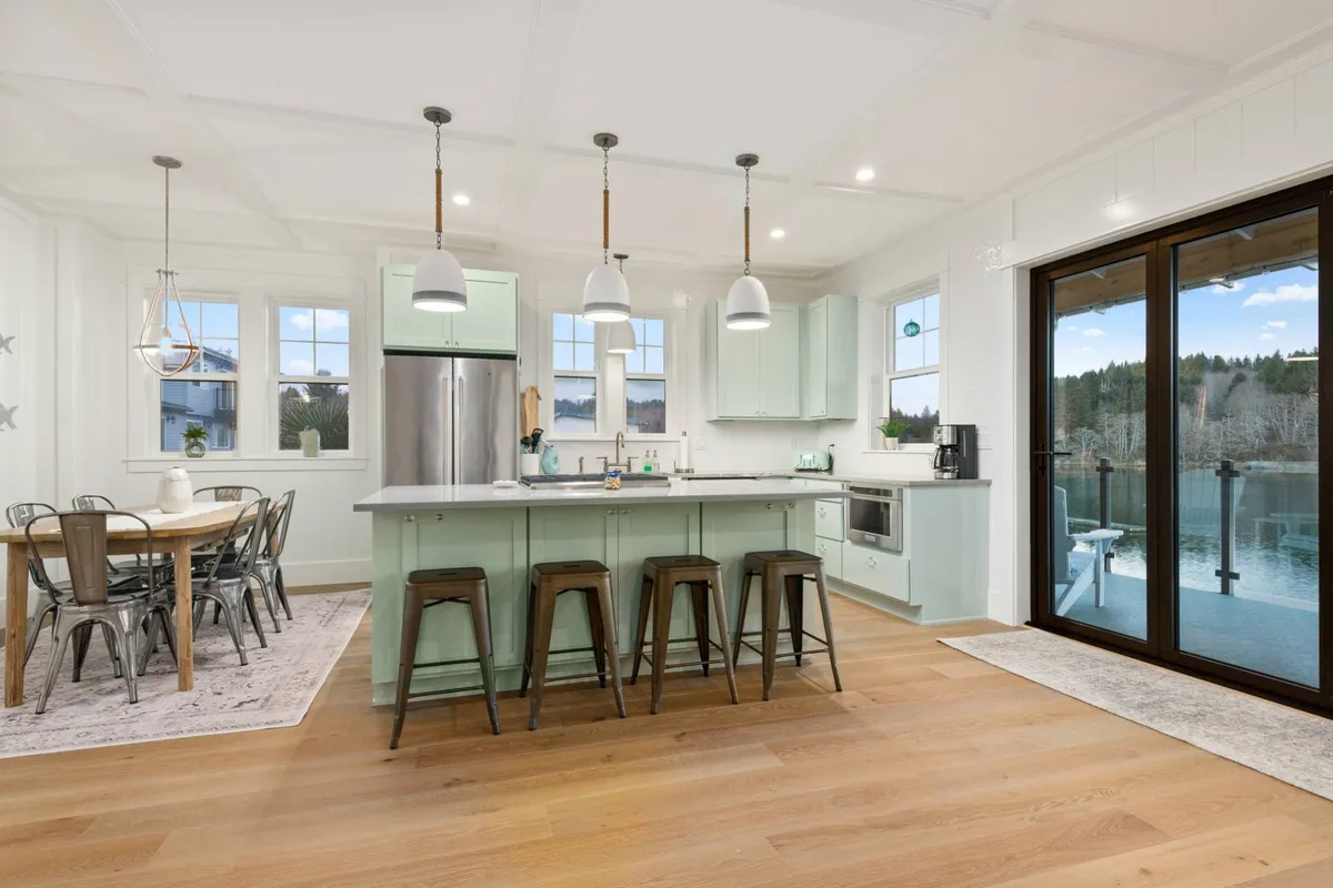 A cohesive view of the kitchen island and the adjacent dining table, framed by large windows that offer a stunning view outside. The image communicates spaciousness and the seamless transition between kitchen and dining areas—ideal for family gatherings or celebratory meals.