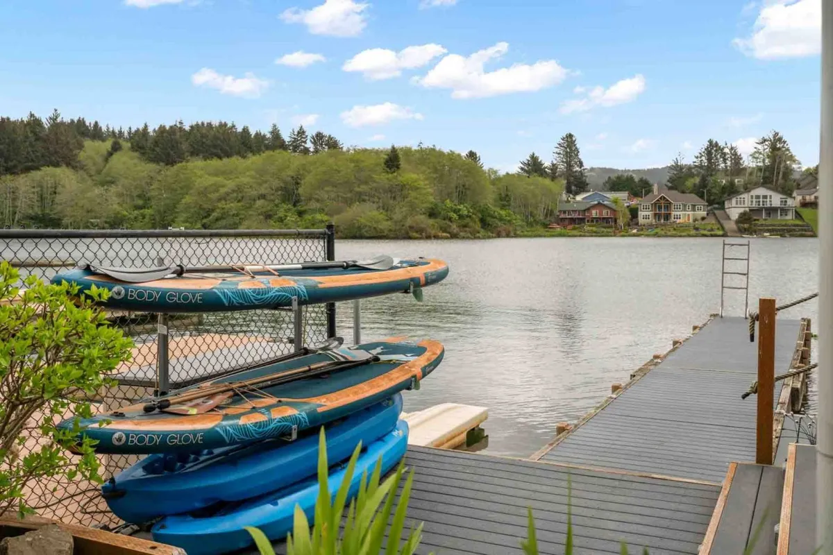 A close-up, energetic view of colorful kayaks lined up on the dock, with the lake just beyond and greenery framing the scene. The image captures the sense of readiness for adventure and water sports right outside the door.