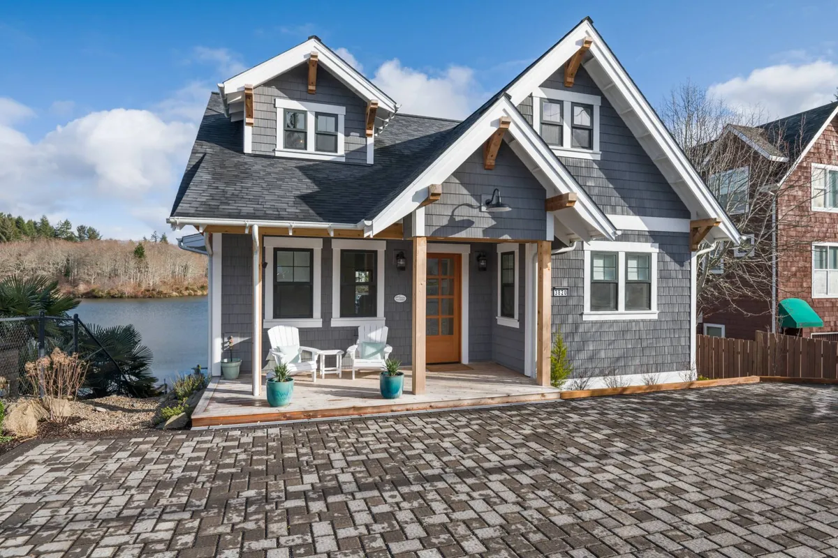 The exterior of a charming house is shown with a welcoming front porch, seating options for relaxation, and a clear view of the lake in the background. The mood is inviting and serene, emphasizing a peaceful retreat.