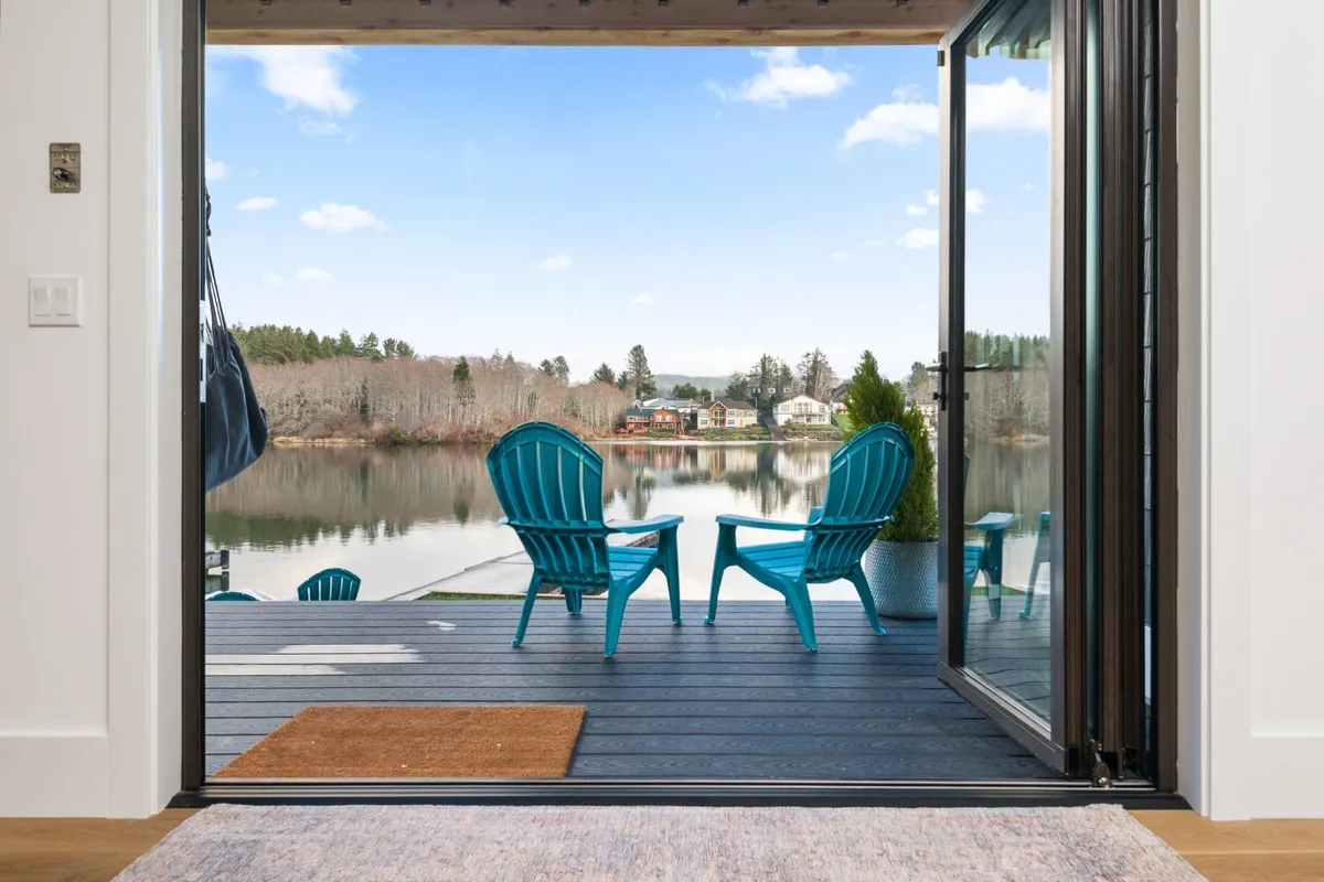 A pair of turquoise chairs are set on a deck overlooking a calm lake, surrounded by natural landscape. The setting is peaceful, ideal for sipping morning coffee, unwinding, or enjoying tranquil conversations at sunrise or sunset.