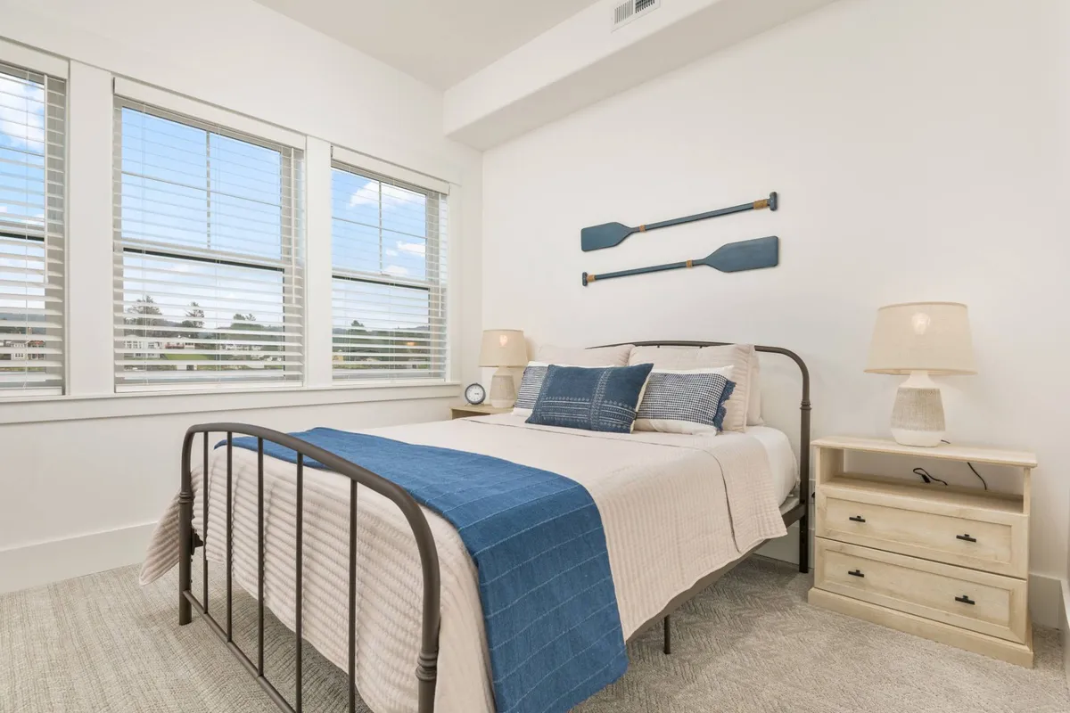 This image features a serene bedroom with blue and white bedding, decorative oars on the wall, and lamps on nightstands. The room feels bright and cozy, perfect for restful nights and peaceful mornings.