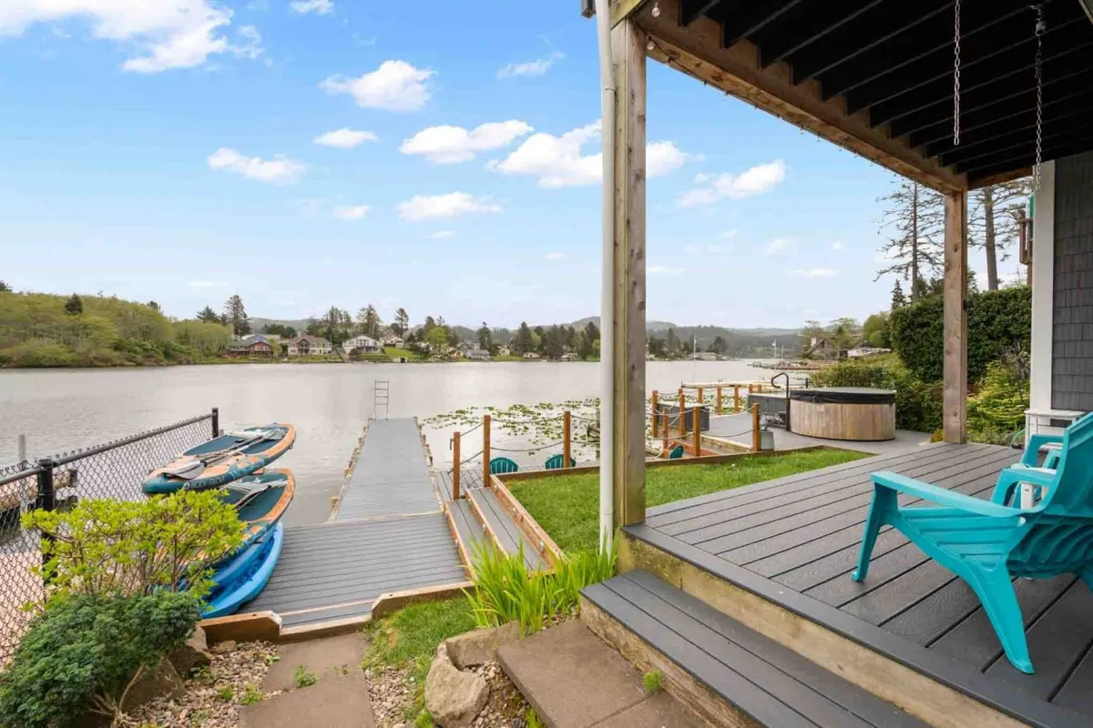 A tranquil lakefront scene featuring a private dock with multiple kayaks, a hot tub, and comfortable seating. The dock directly accesses the water, surrounded by lush greenery and calm waters, perfectly highlighting opportunities for kayaking, fishing, and relaxation.