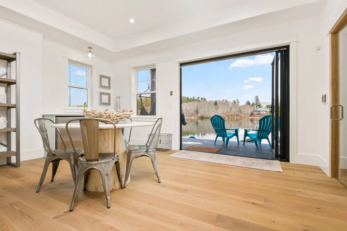 A bright dining area with blue chairs surrounding a large table, facing expansive openings to the outdoors. The image captures how the interior seamlessly connects with the outside, reinforcing the effect of Nano doors mentioned in the narrative.